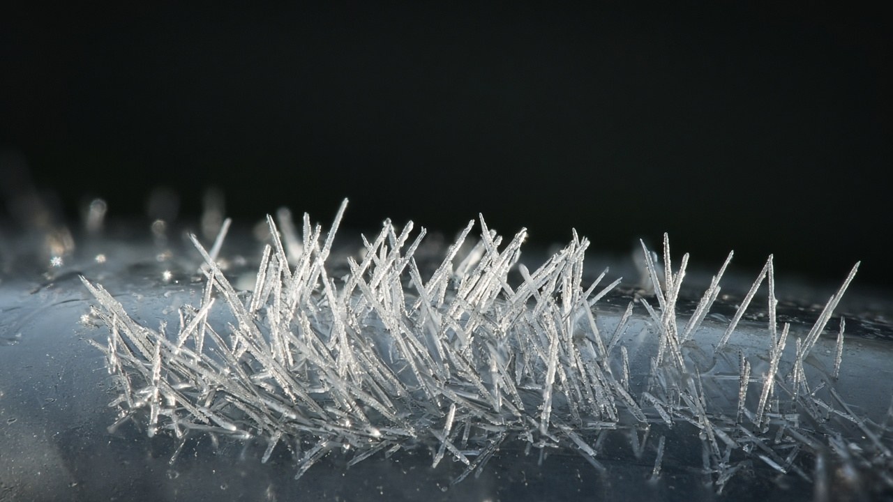 Close-up illustration of white needle-shaped crystals growing on glass against a dark background